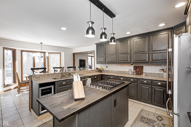 kitchen with appliances with stainless steel finishes, a kitchen island, butcher block counters, hanging light fixtures, and kitchen peninsula