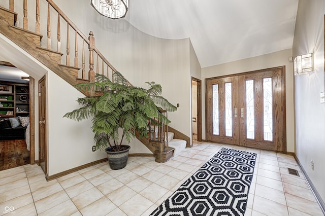 foyer entrance featuring high vaulted ceiling, light tile patterned floors, french doors, and an inviting chandelier