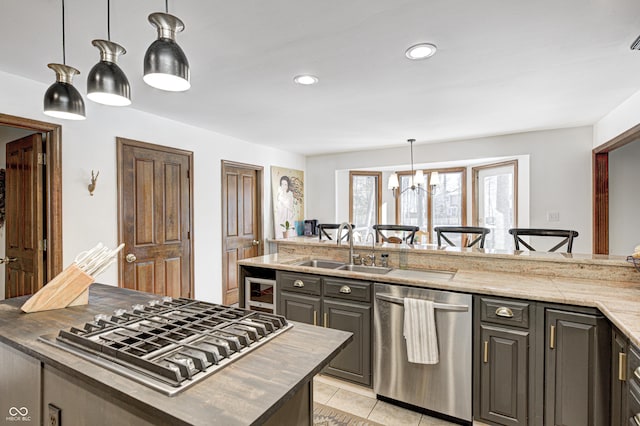 kitchen with appliances with stainless steel finishes, a center island, a notable chandelier, light stone counters, and sink