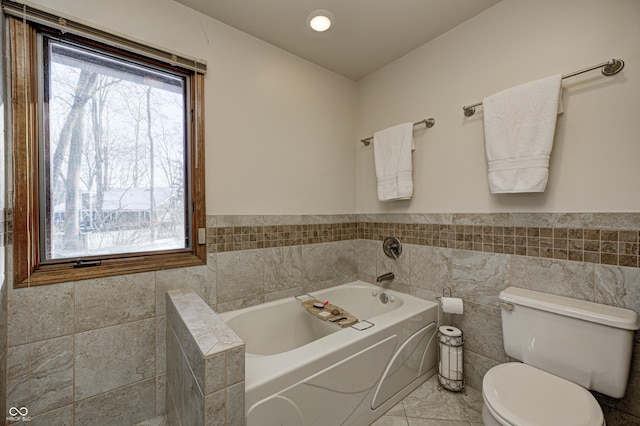 bathroom with tile walls, toilet, and a tub to relax in