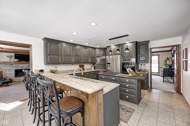 kitchen with kitchen peninsula, appliances with stainless steel finishes, hanging light fixtures, dark stone counters, and sink