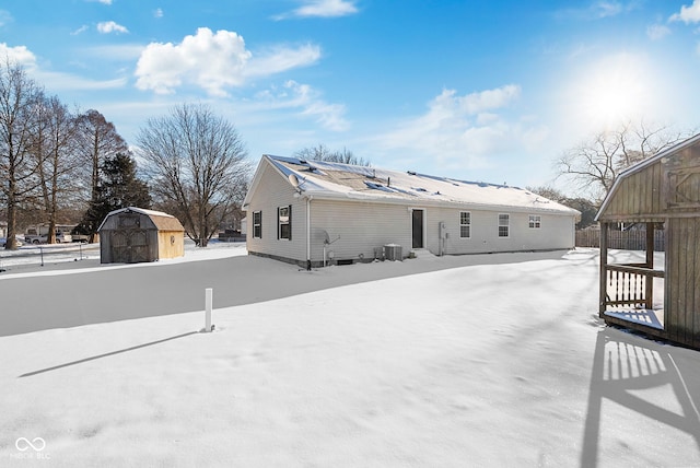 snow covered back of property featuring central AC unit and a shed