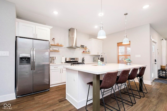 kitchen with wall chimney range hood, sink, an island with sink, appliances with stainless steel finishes, and white cabinetry