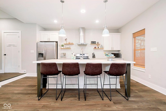 kitchen featuring a breakfast bar, stainless steel fridge, white cabinetry, and wall chimney range hood