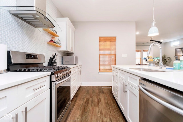 kitchen featuring wall chimney exhaust hood, stainless steel appliances, sink, decorative light fixtures, and white cabinetry