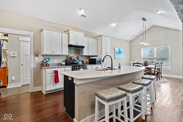 kitchen with pendant lighting, vaulted ceiling, white cabinetry, and gas range