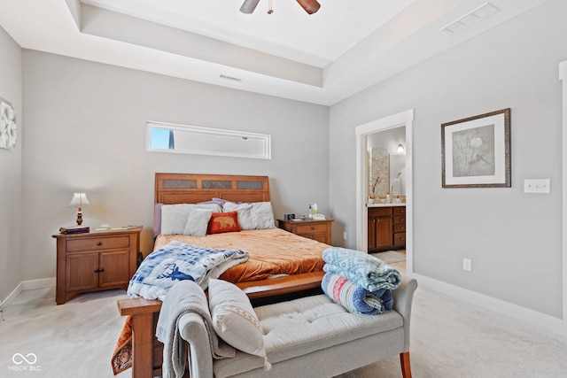 bedroom featuring a tray ceiling, ensuite bath, ceiling fan, and light colored carpet