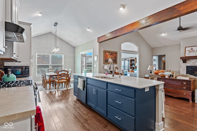 kitchen with a center island with sink, a stone fireplace, blue cabinets, sink, and decorative light fixtures