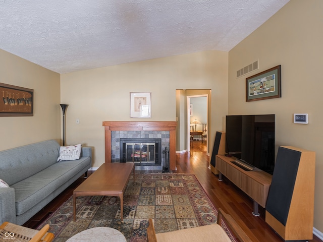 living room with dark hardwood / wood-style flooring, a textured ceiling, and a tiled fireplace