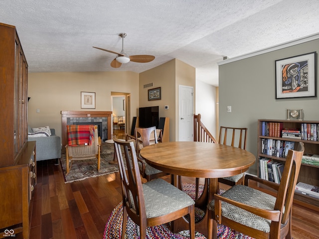 dining area with dark wood-type flooring, vaulted ceiling, ceiling fan, a textured ceiling, and a tiled fireplace