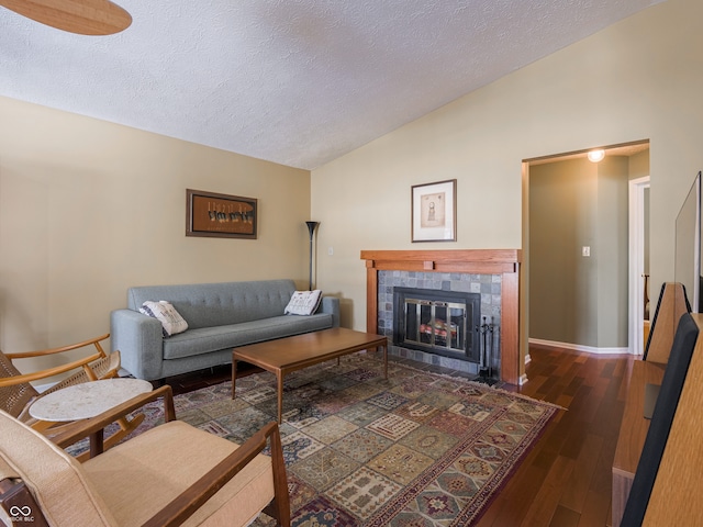 living room with a textured ceiling, vaulted ceiling, dark wood-type flooring, and a tiled fireplace