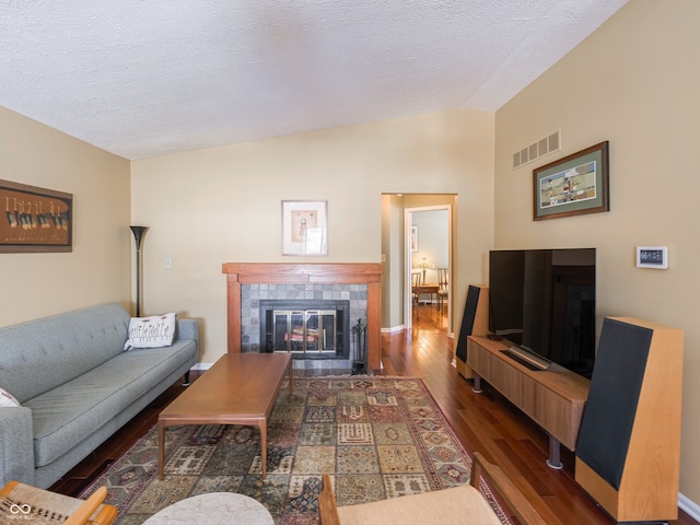 living room featuring visible vents, vaulted ceiling, a fireplace, wood finished floors, and a textured ceiling