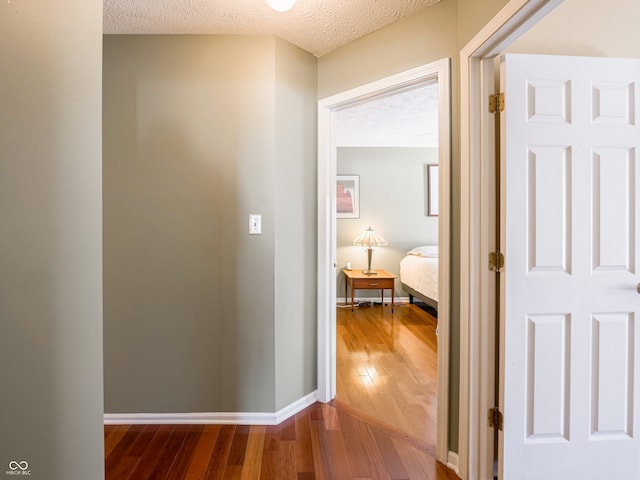 hall with a textured ceiling, baseboards, and wood-type flooring