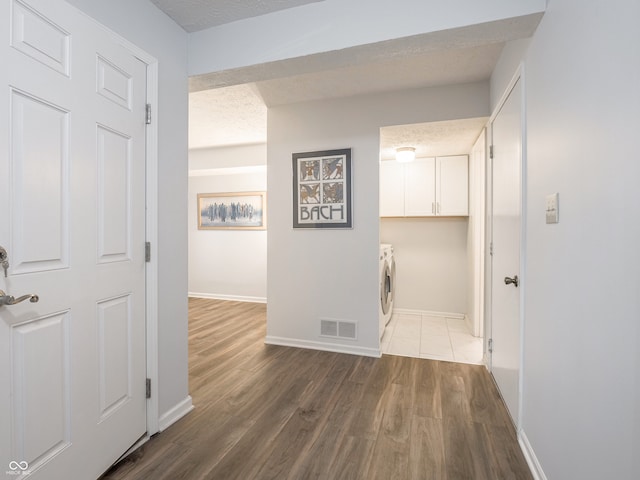 hallway featuring washing machine and dryer, a textured ceiling, baseboards, and wood finished floors