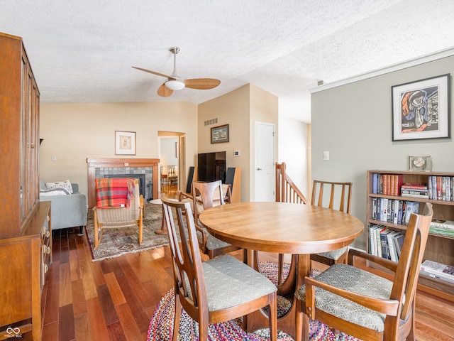 dining space featuring visible vents, ceiling fan, a tiled fireplace, vaulted ceiling, and wood finished floors