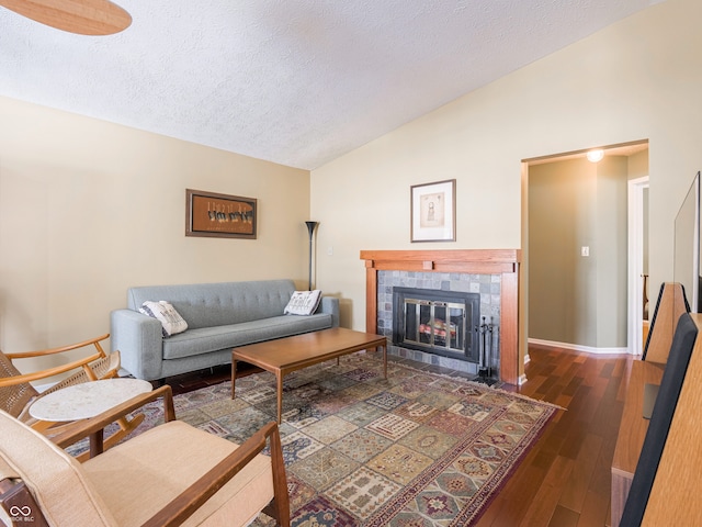 living area featuring baseboards, hardwood / wood-style floors, vaulted ceiling, a fireplace, and a textured ceiling