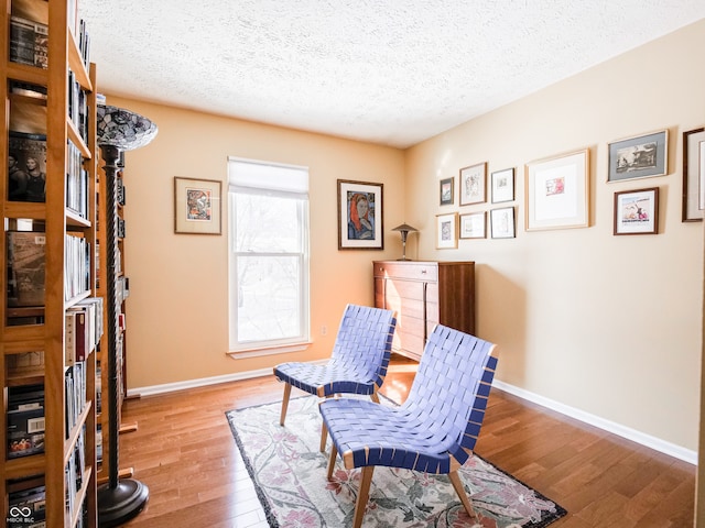 living area featuring a textured ceiling, baseboards, and hardwood / wood-style flooring