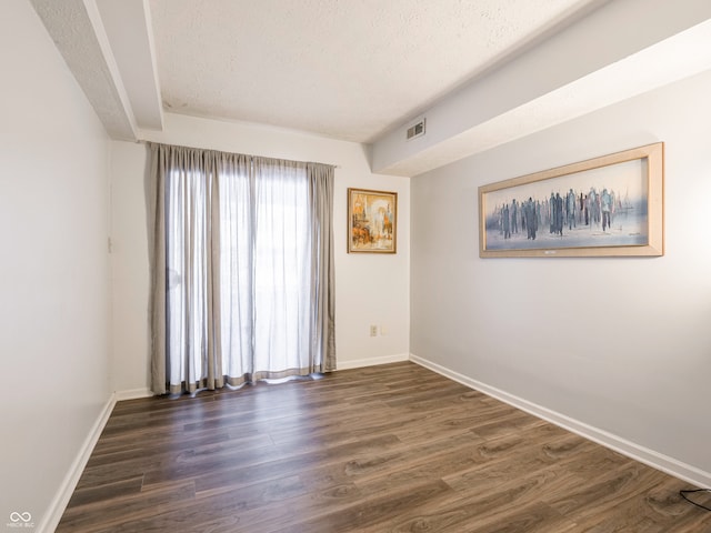 unfurnished room featuring visible vents, baseboards, a textured ceiling, and dark wood finished floors