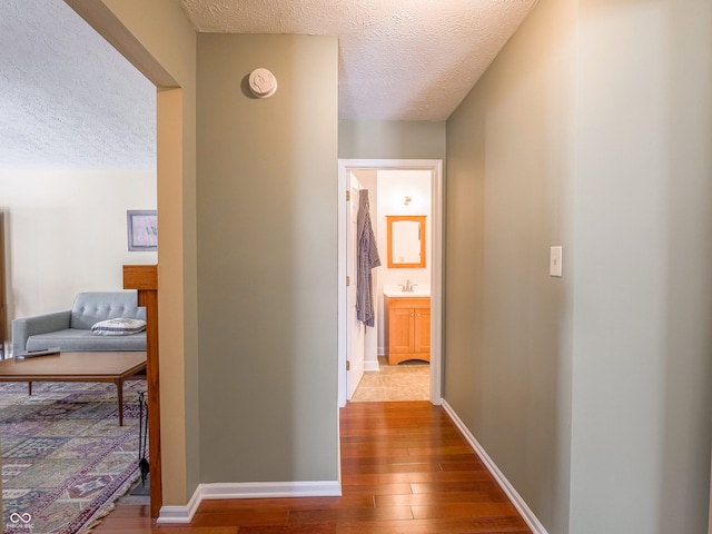 hallway with a sink, baseboards, a textured ceiling, and wood finished floors