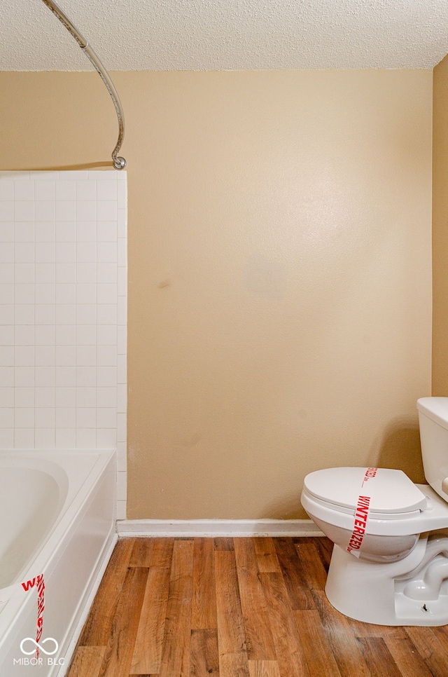 bathroom featuring toilet, a textured ceiling, hardwood / wood-style floors, and washtub / shower combination