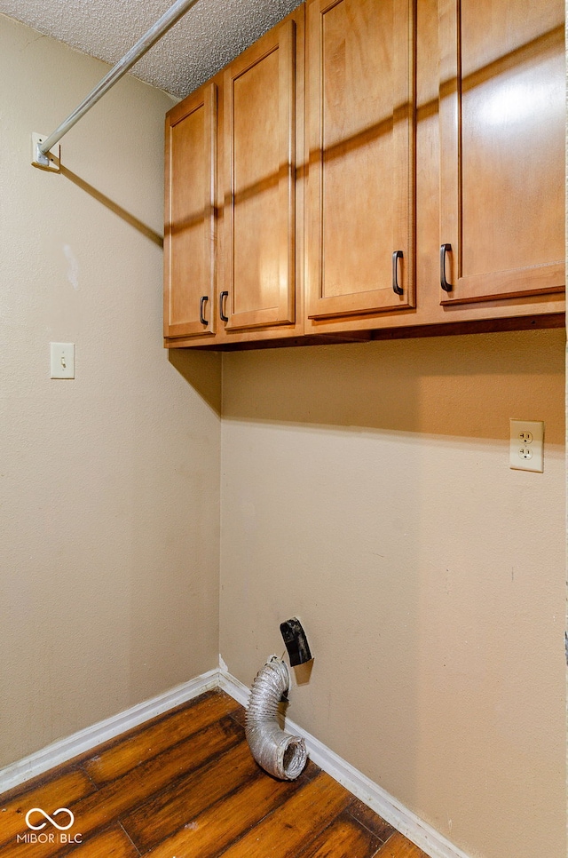 clothes washing area with a textured ceiling, cabinets, and dark hardwood / wood-style floors