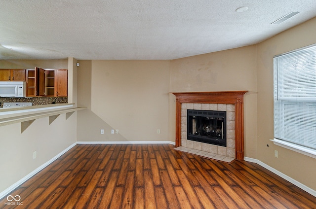 unfurnished living room featuring a tile fireplace, a textured ceiling, and dark wood-type flooring