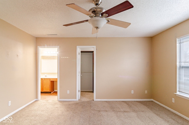 unfurnished bedroom featuring ensuite bathroom, a spacious closet, light carpet, ceiling fan, and a closet