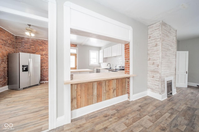 kitchen featuring a large fireplace, brick wall, kitchen peninsula, light hardwood / wood-style floors, and appliances with stainless steel finishes