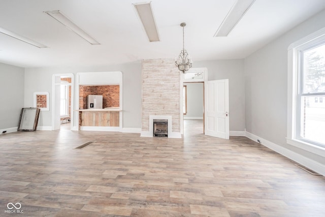 unfurnished living room featuring a large fireplace, light hardwood / wood-style floors, an inviting chandelier, and a healthy amount of sunlight