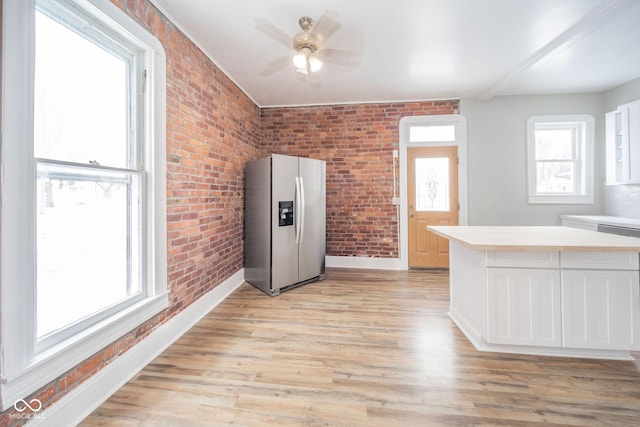 kitchen featuring white cabinets, stainless steel fridge, brick wall, and light hardwood / wood-style flooring