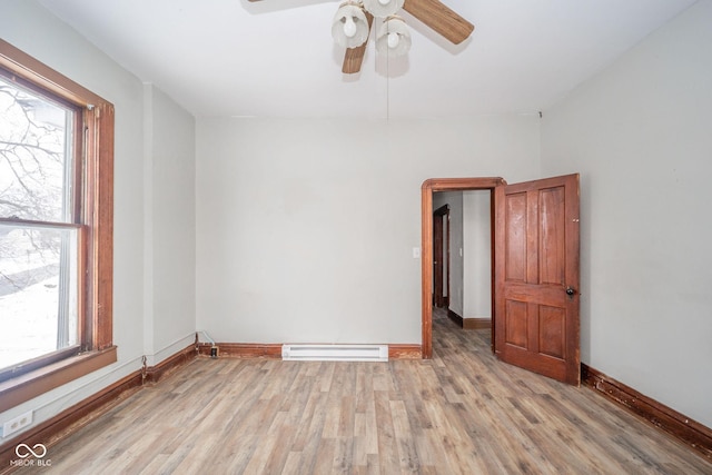 empty room featuring light wood-type flooring, plenty of natural light, a baseboard heating unit, and ceiling fan