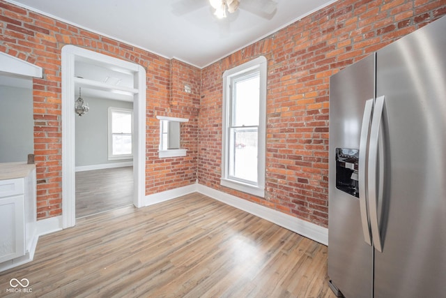 kitchen with white cabinets, ceiling fan with notable chandelier, light wood-type flooring, stainless steel fridge with ice dispenser, and brick wall