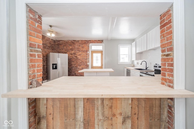 kitchen with sink, stainless steel appliances, brick wall, kitchen peninsula, and white cabinets