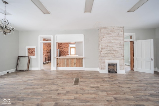 unfurnished living room featuring a fireplace, wood-type flooring, and an inviting chandelier