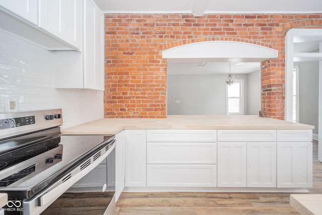 kitchen with white cabinetry, brick wall, backsplash, decorative light fixtures, and stainless steel electric stove