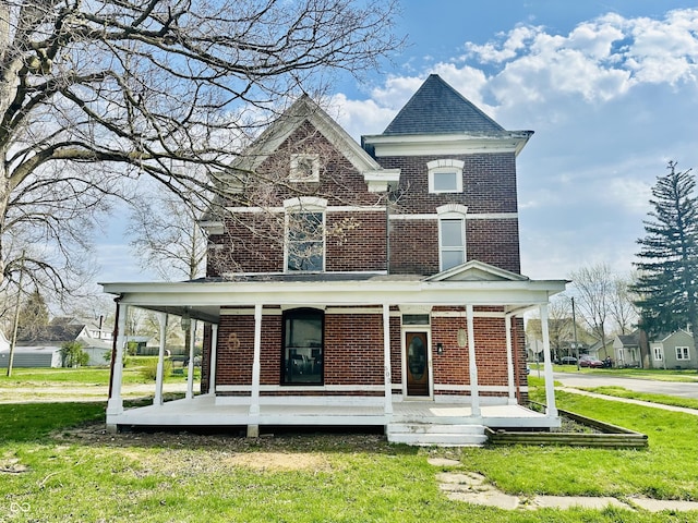 victorian-style house featuring a front lawn, brick siding, and a porch