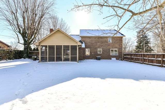 snow covered house featuring central air condition unit and a sunroom