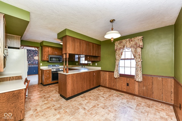 kitchen with electric range, sink, hanging light fixtures, kitchen peninsula, and wood walls