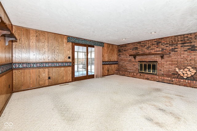 unfurnished living room with a textured ceiling, wood walls, light colored carpet, and a fireplace