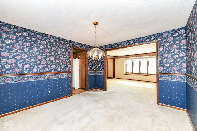 spare room featuring carpet, a textured ceiling, and an inviting chandelier