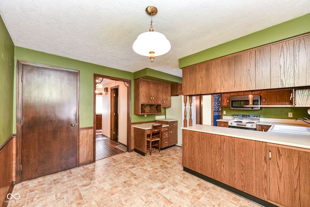 kitchen featuring sink, wooden walls, appliances with stainless steel finishes, decorative light fixtures, and kitchen peninsula