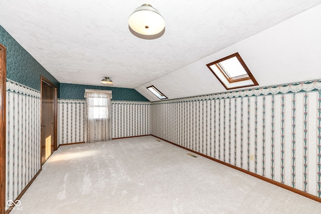 bonus room featuring vaulted ceiling with skylight, carpet floors, and a textured ceiling