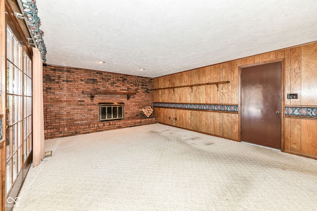 unfurnished living room with wooden walls, a fireplace, carpet, and a textured ceiling