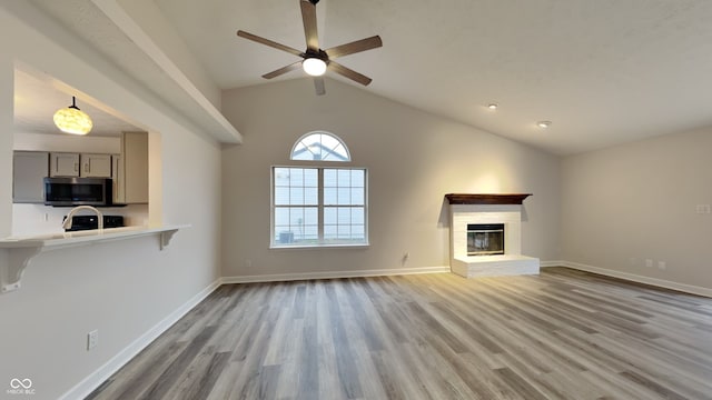 unfurnished living room featuring light hardwood / wood-style flooring, a brick fireplace, ceiling fan, and lofted ceiling