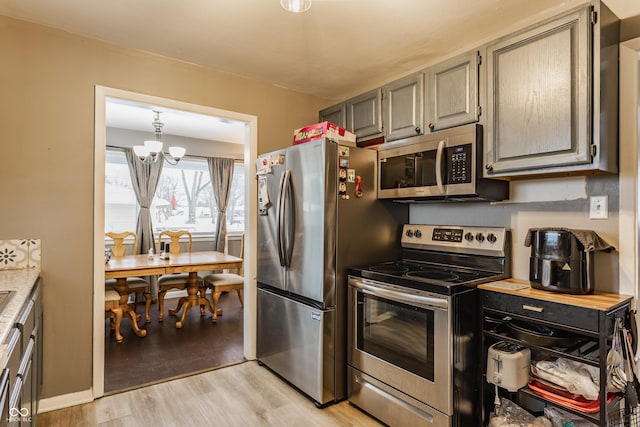 kitchen featuring a chandelier, decorative light fixtures, gray cabinets, appliances with stainless steel finishes, and light wood-type flooring