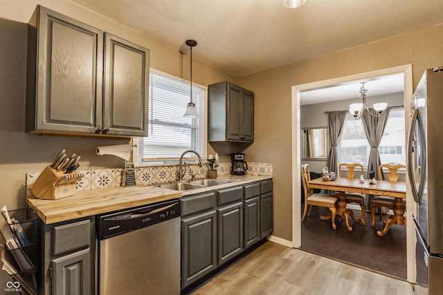 kitchen featuring pendant lighting, sink, light wood-type flooring, stainless steel appliances, and a chandelier