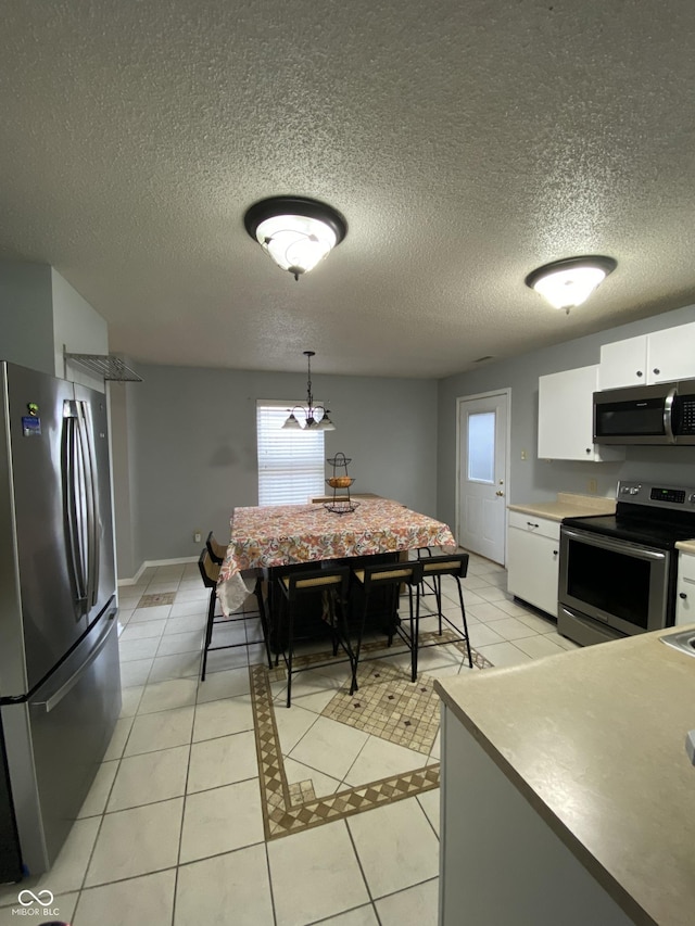 kitchen featuring pendant lighting, stainless steel appliances, white cabinetry, and light tile patterned flooring