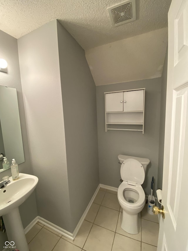 bathroom featuring vaulted ceiling, tile patterned flooring, a textured ceiling, and toilet