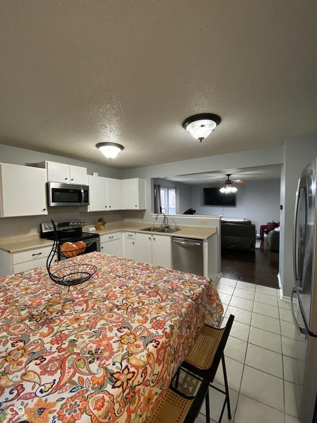 kitchen featuring kitchen peninsula, ceiling fan, light tile patterned floors, white cabinetry, and stainless steel appliances