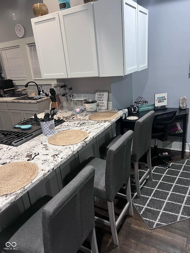 kitchen with light stone counters, white cabinetry, sink, and dark wood-type flooring